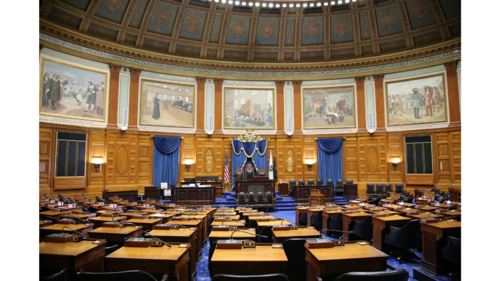 Interior of a state legislative chamber with desks, flags, and ornate walls